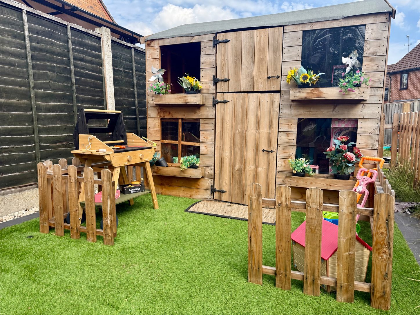 Our two-storey wooden playhouse with flower boxes, play barbecue and picket-fenced play areas